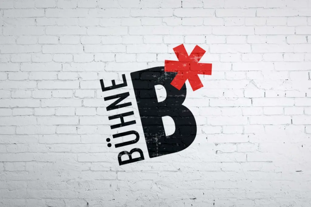 Logo von B-Bühne mit schwarzer Schrift und rotem Sternchen auf einer weißen Backsteinwand