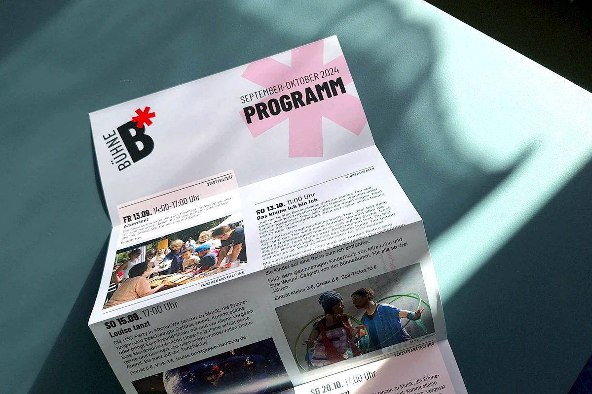 Ein gefaltetes Programmheft der Bühne B* für September und Oktober 2024 liegt auf einem Tisch. Es enthält Veranstaltungsdetails, Bilder und Texte zu verschiedenen Events